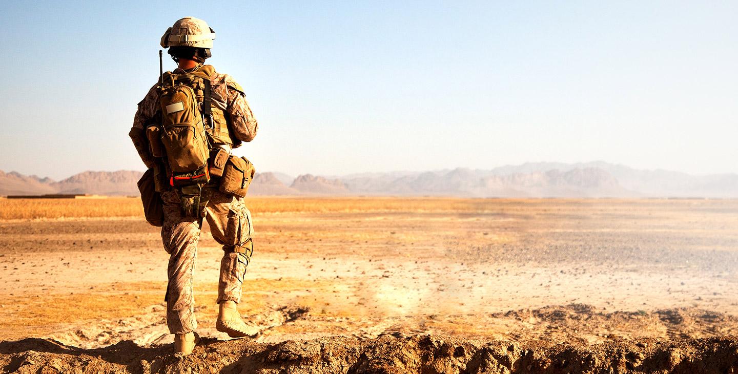 沙漠里一个士兵的背影，穿着军服，背着背包